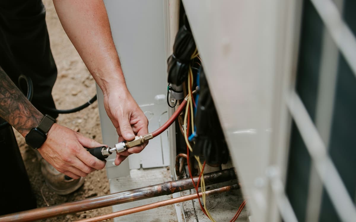 A technician connects a refrigerant gauge hose to an outdoor air conditioning unit.